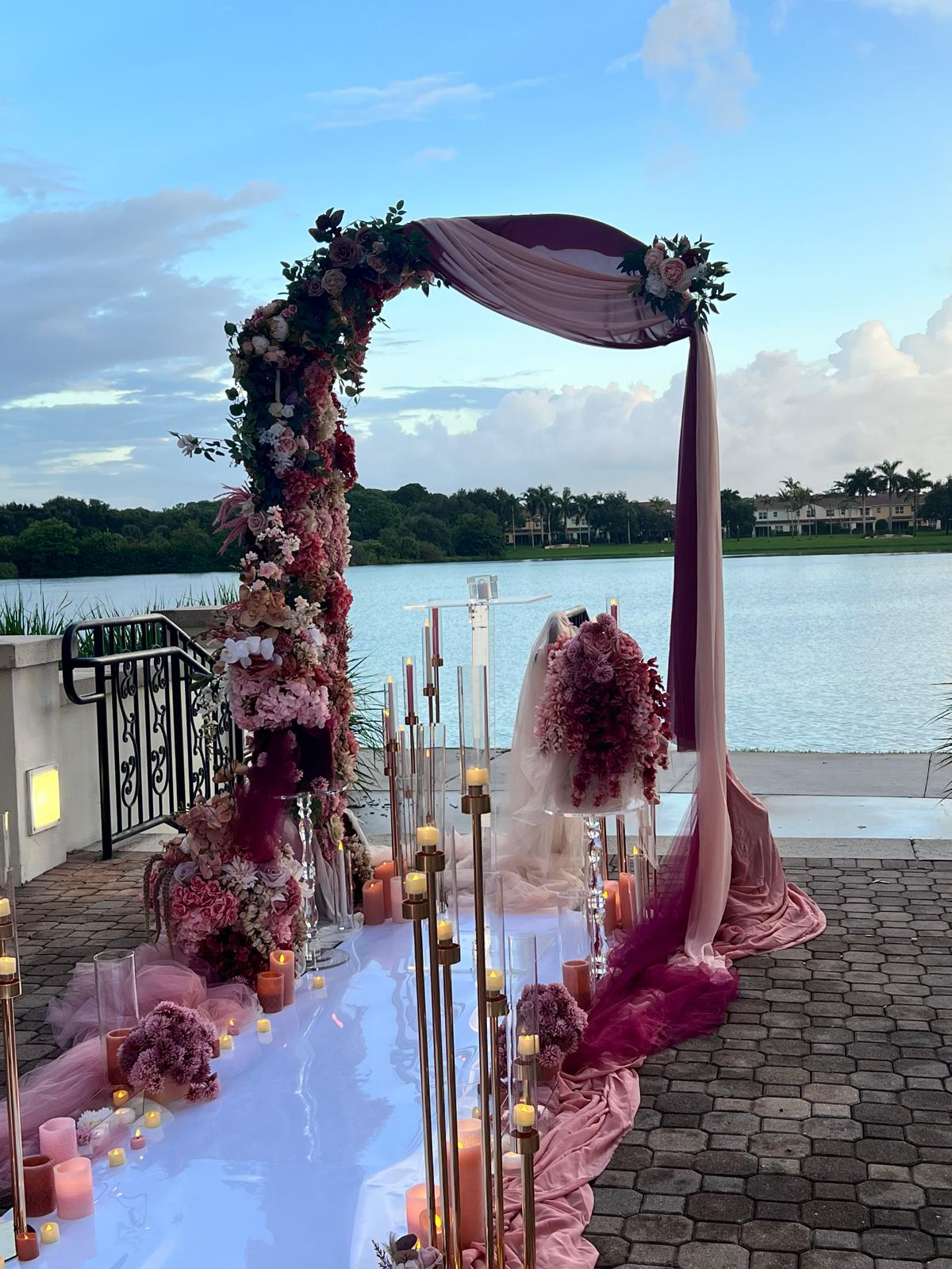 Crimson Vows burgundy and blush floral arch beside the water